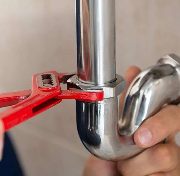 Artisan plombier professionnel intervenant sur un raccordement de tuyauterie avec une clé de serrage.